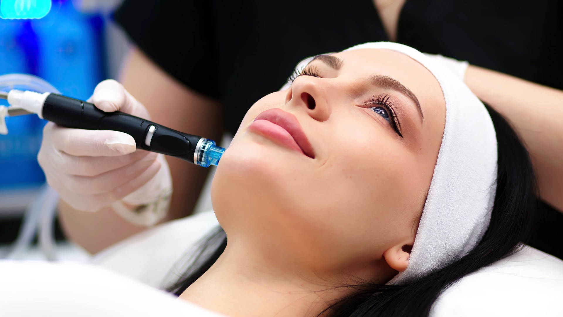 Anti-aging care, skin care, facial cleansing. A cosmetologist does a hydrofacial procedure on a woman's face in a beauty clinic.